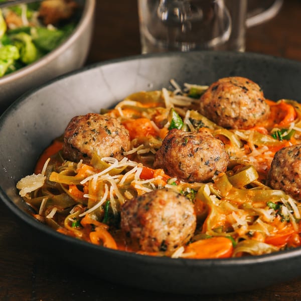 Meatballs and pasta in a creamy orange sauce, topped with shredded cheese and herbs.