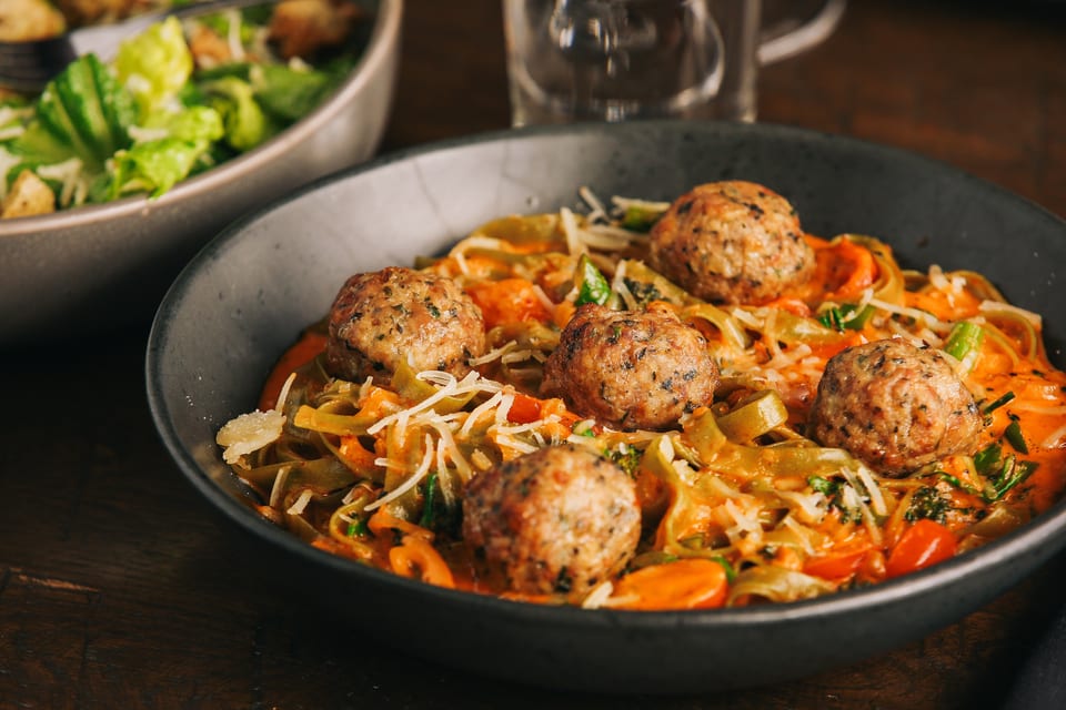 Meatballs and pasta in a creamy orange sauce, topped with shredded cheese and herbs.