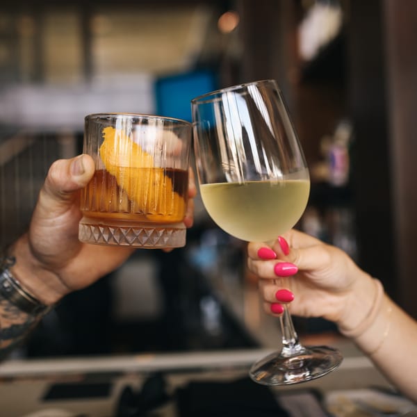 Two people toast with a cocktail and a glass of white wine in a restaurant.