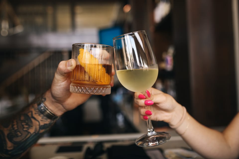 Two people toast with a cocktail and a glass of white wine in a restaurant.