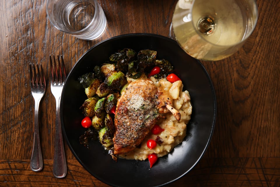 Crispy chicken with roasted Brussels sprouts, mashed potatoes, and cherry tomatoes on a dark plate.