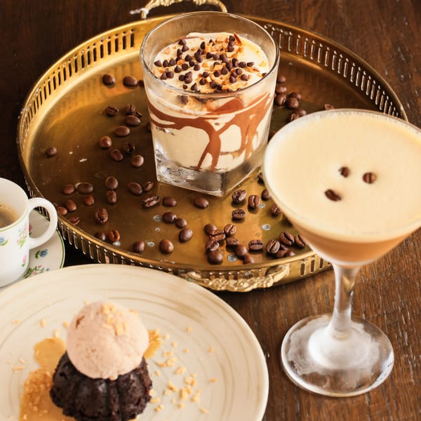 Dessert spread with chocolate lava cake, ice cream, coffee drinks, and coffee beans on a wooden table.