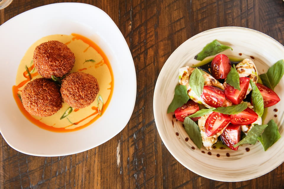 Two dishes on a wooden table: fried arancini in sauce and a caprese salad with tomatoes, mozzarella, and basil.
